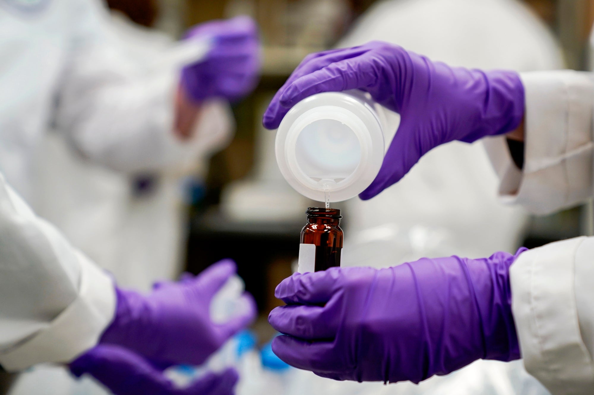 A close up of rubber gloved hands pouring water from one container to another in a laboratory.