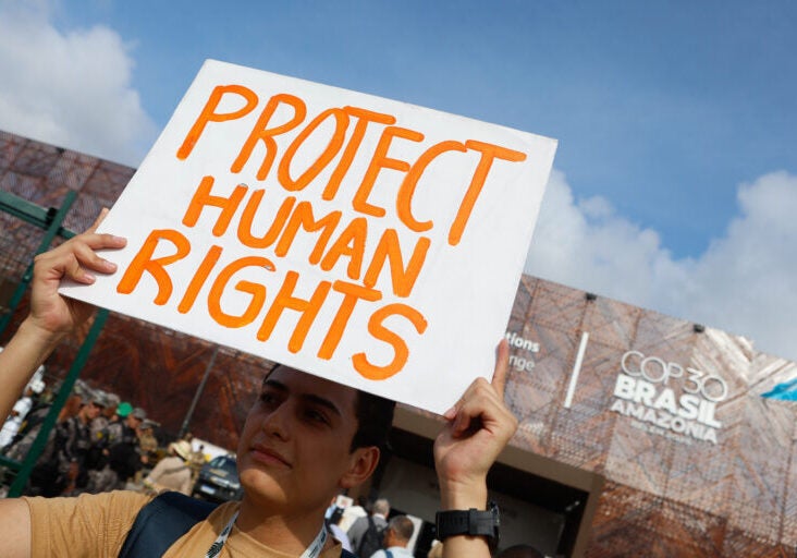 A man holds a sign that says "Protect Human Rights" at a civil society demonstration at the COP30 in Belém, Brazil.