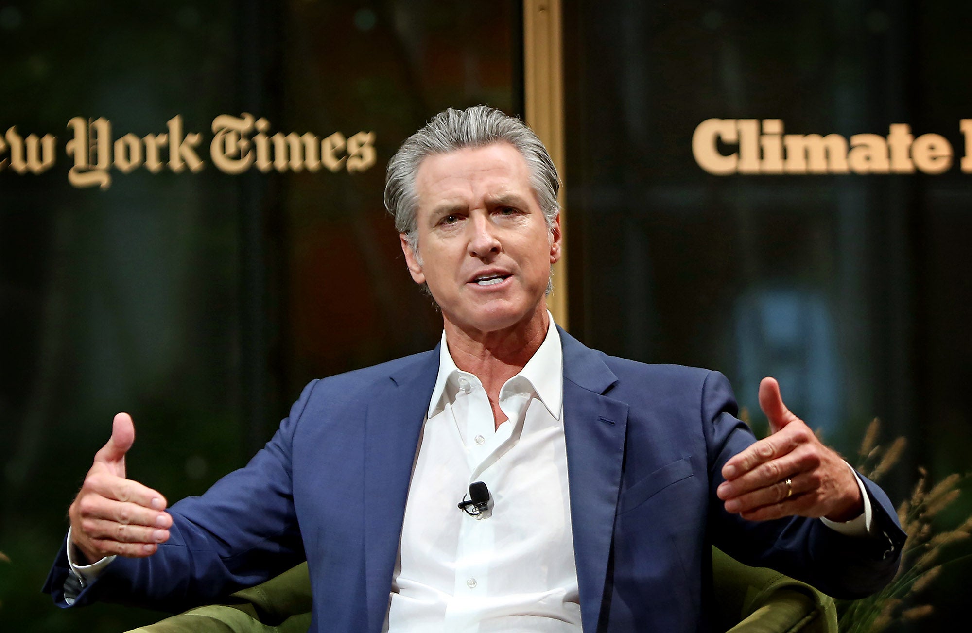 Gavin Newsom, wearing a blue sports jacket and white shirt gestures with both hands while speaking.