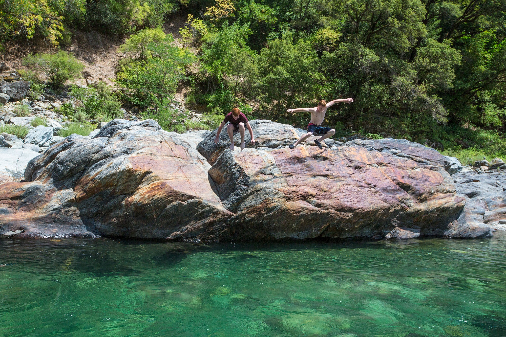 Two young swimmers leap from a large boulder into the pristine waters of the North Fork of the American River.