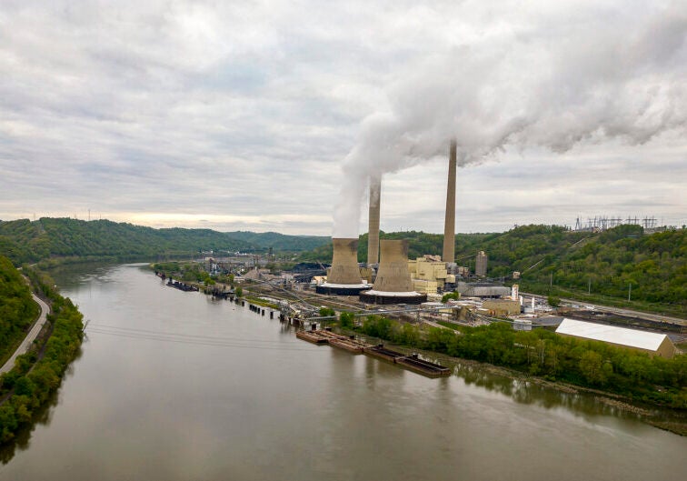 A coal power plant emitting smoke on the bank on the curve of a river.