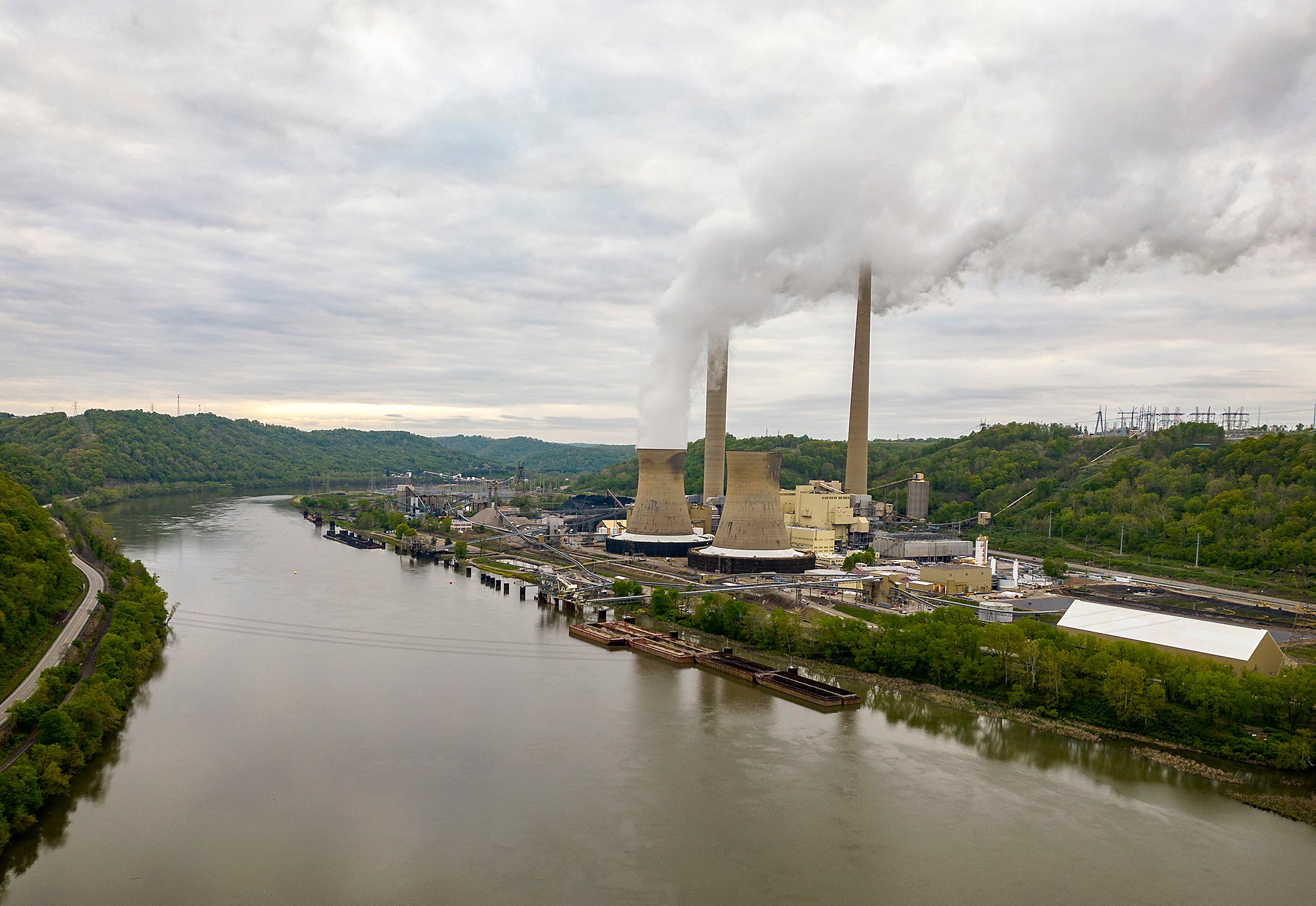 A coal power plant emitting smoke on the bank on the curve of a river.