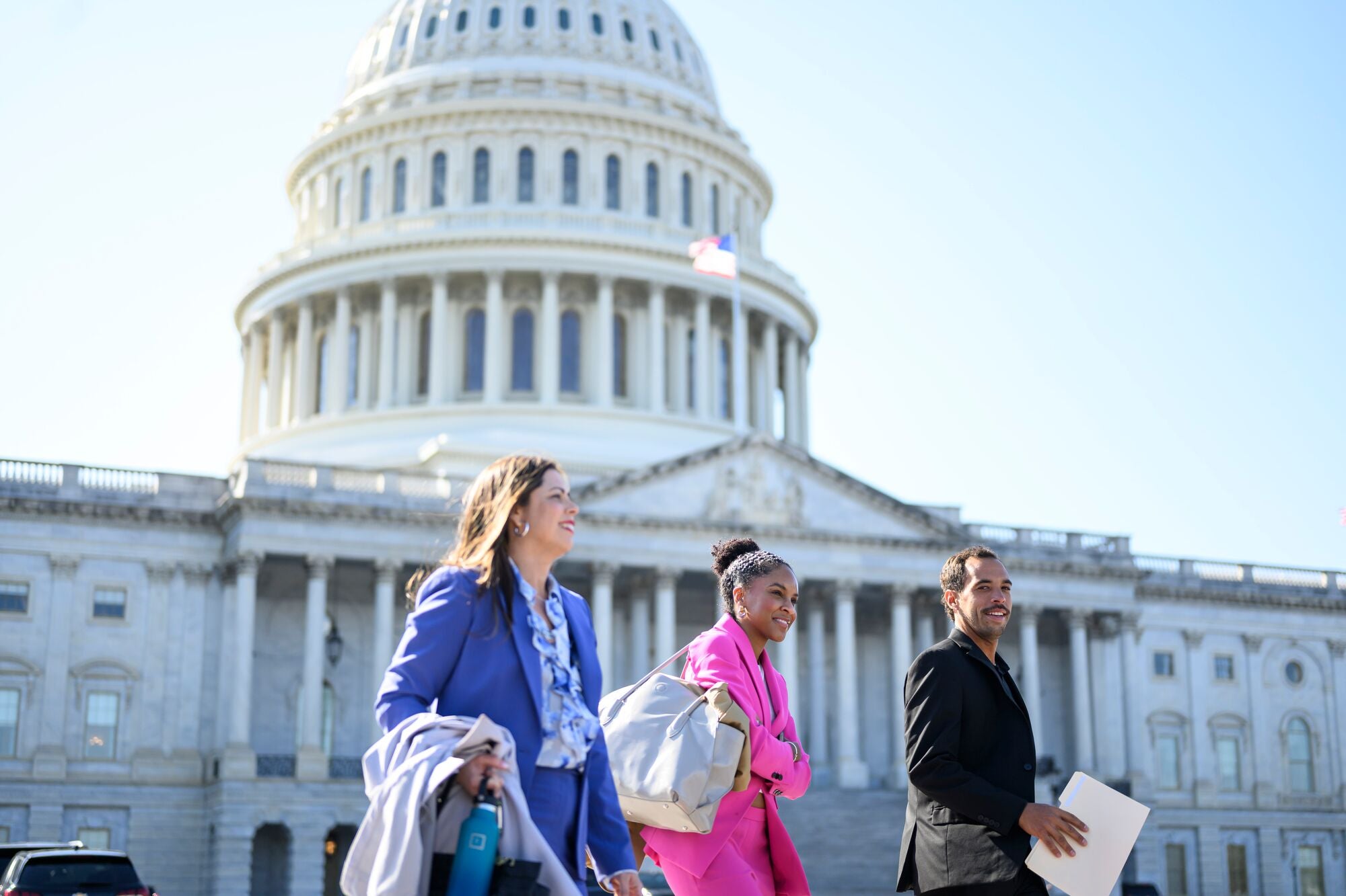 Members of Earthjustice and El Puente cheerfully walk out from the main entrance of the U.S. Capitol building, with the U.S. flag flying in front of the building's classic rotunda, on a bright sunny day.
